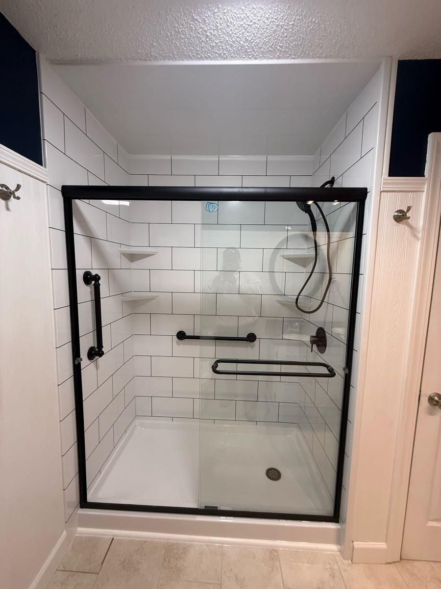 Accessible bathroom shower with black frame, white subway tile, and grab bars.