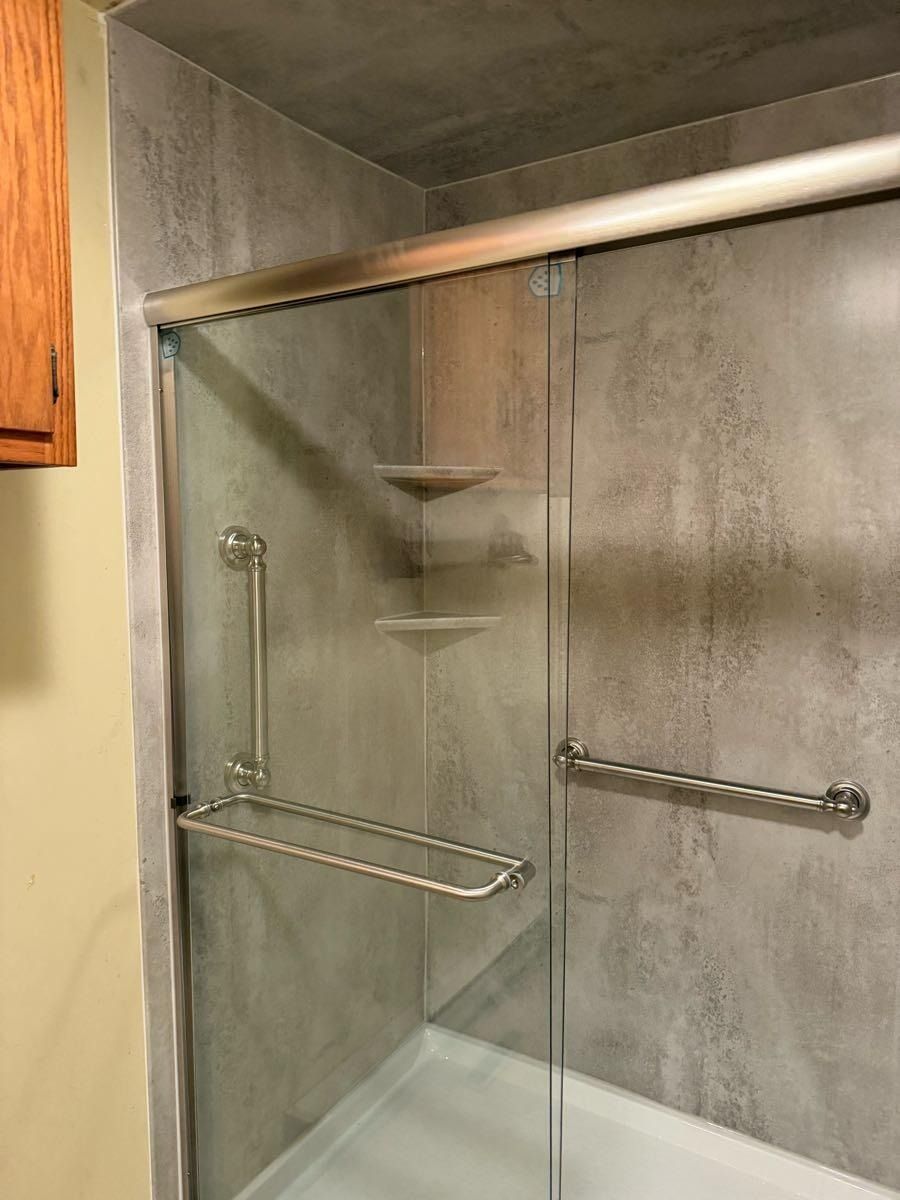 Gray tiled shower with glass door and silver grab bars.
