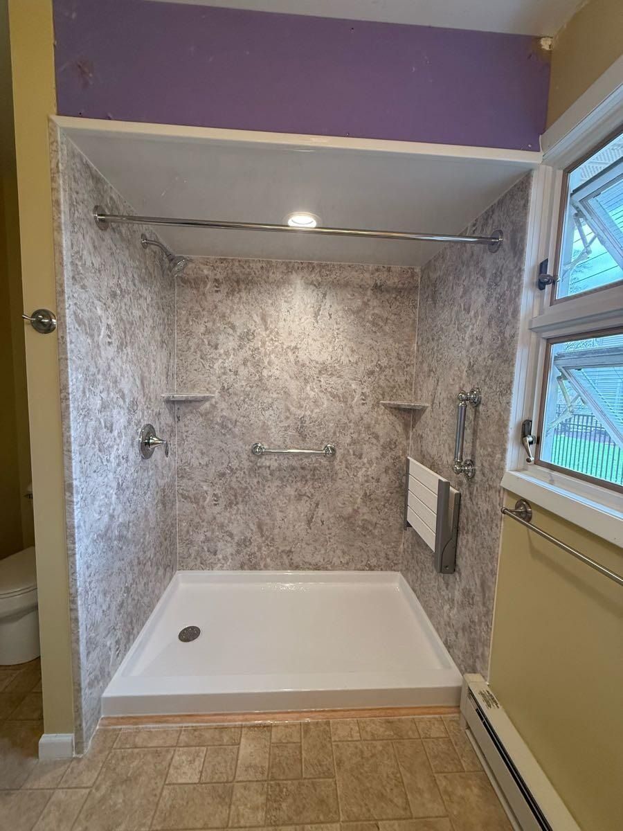 Bathroom with white shower basin, gray and white shower walls, silver fixtures, and a window.