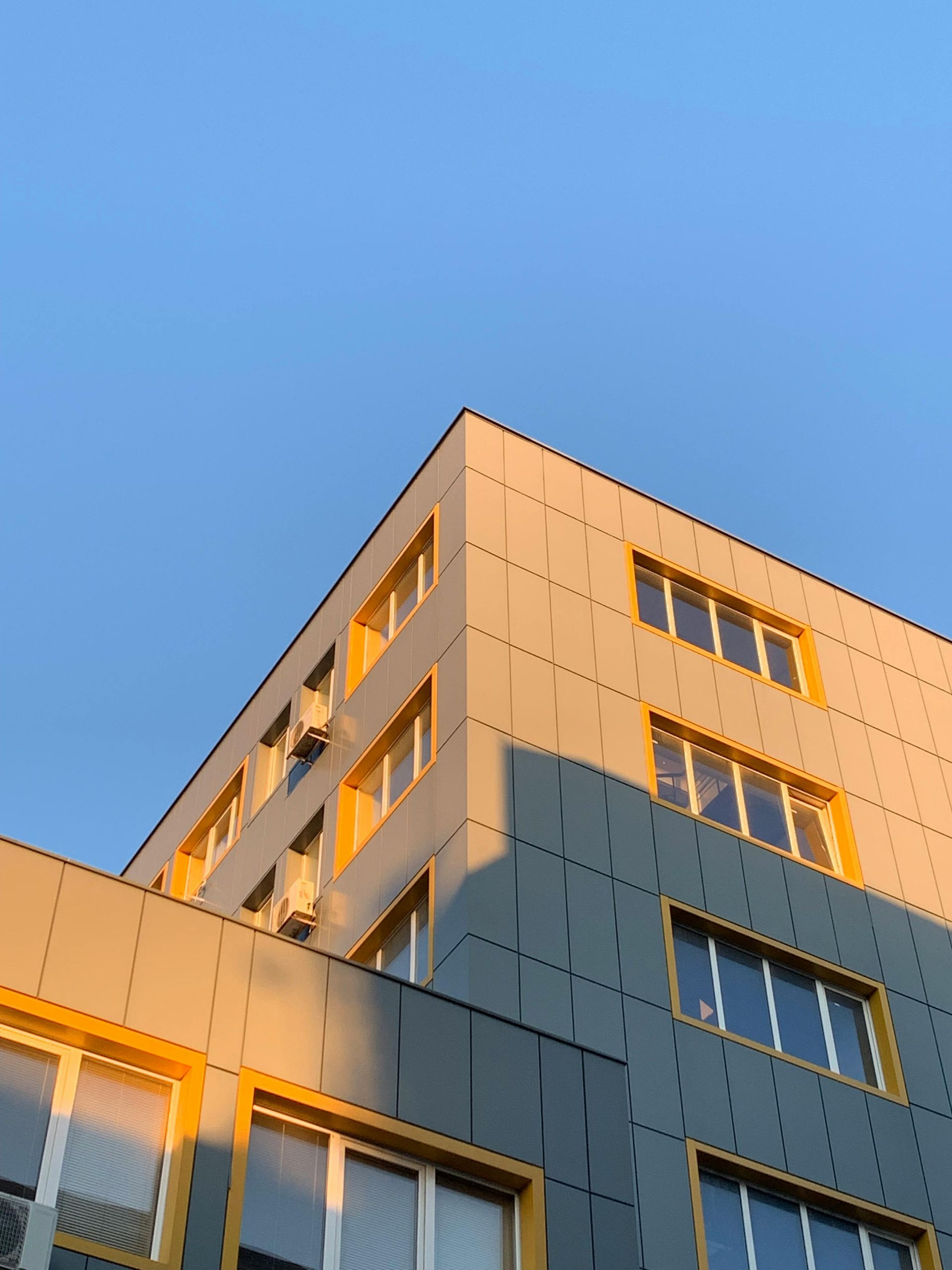 Corner of a modern building with yellow-framed windows and a blue sky in the background.