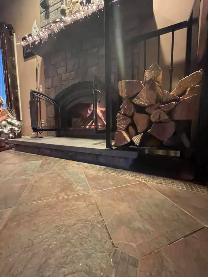 Cozy fireplace with burning logs, stacked firewood, and a patterned tile floor in a rustic room