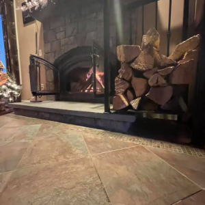 Cozy fireplace with burning fire, stacked firewood, and stone-tile floor in a rustic room