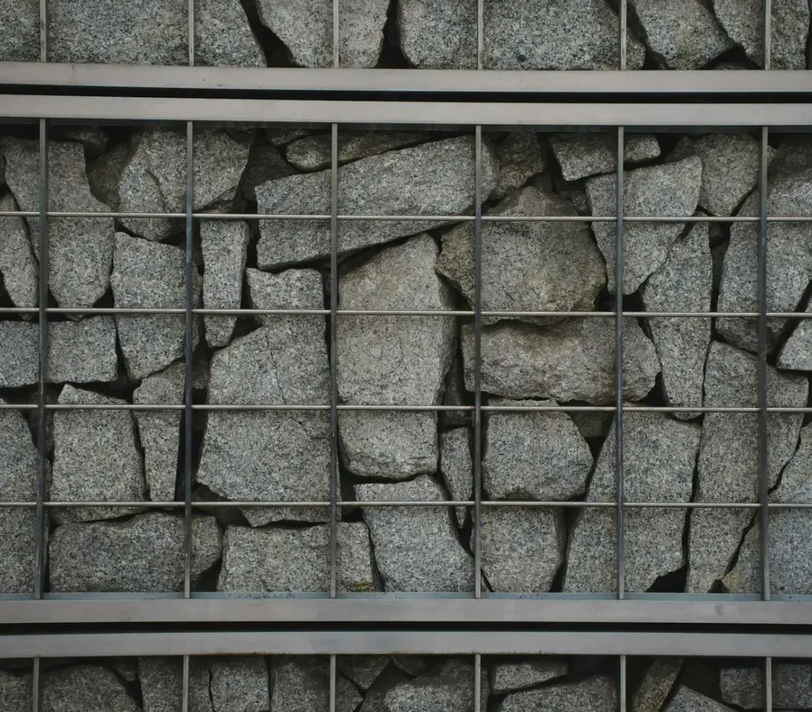 Gray stone wall with a grid of dark metal bars over broken, uneven stone panels