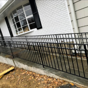 Black metal ramp railing along a white brick house exterior, beside a window and fallen leaves.