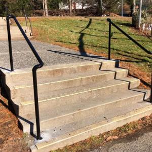 Concrete outdoor stairs with black metal handrails beside a grassy area and sidewalk.