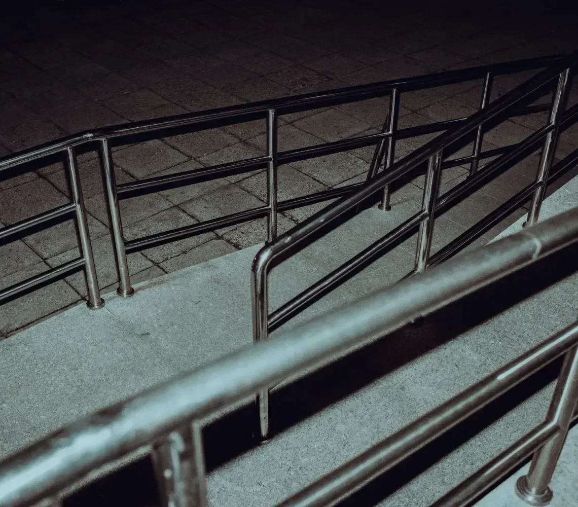 Metal railings along a sloped concrete ramp at night, viewed from above.