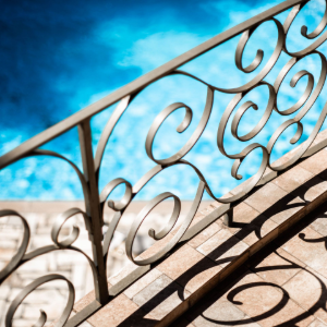 Curved wrought-iron stair railing casting shadows beside a blue water background