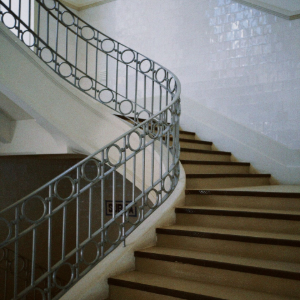 Curving indoor staircase with brown steps and ornate gray metal railing against white tiled walls