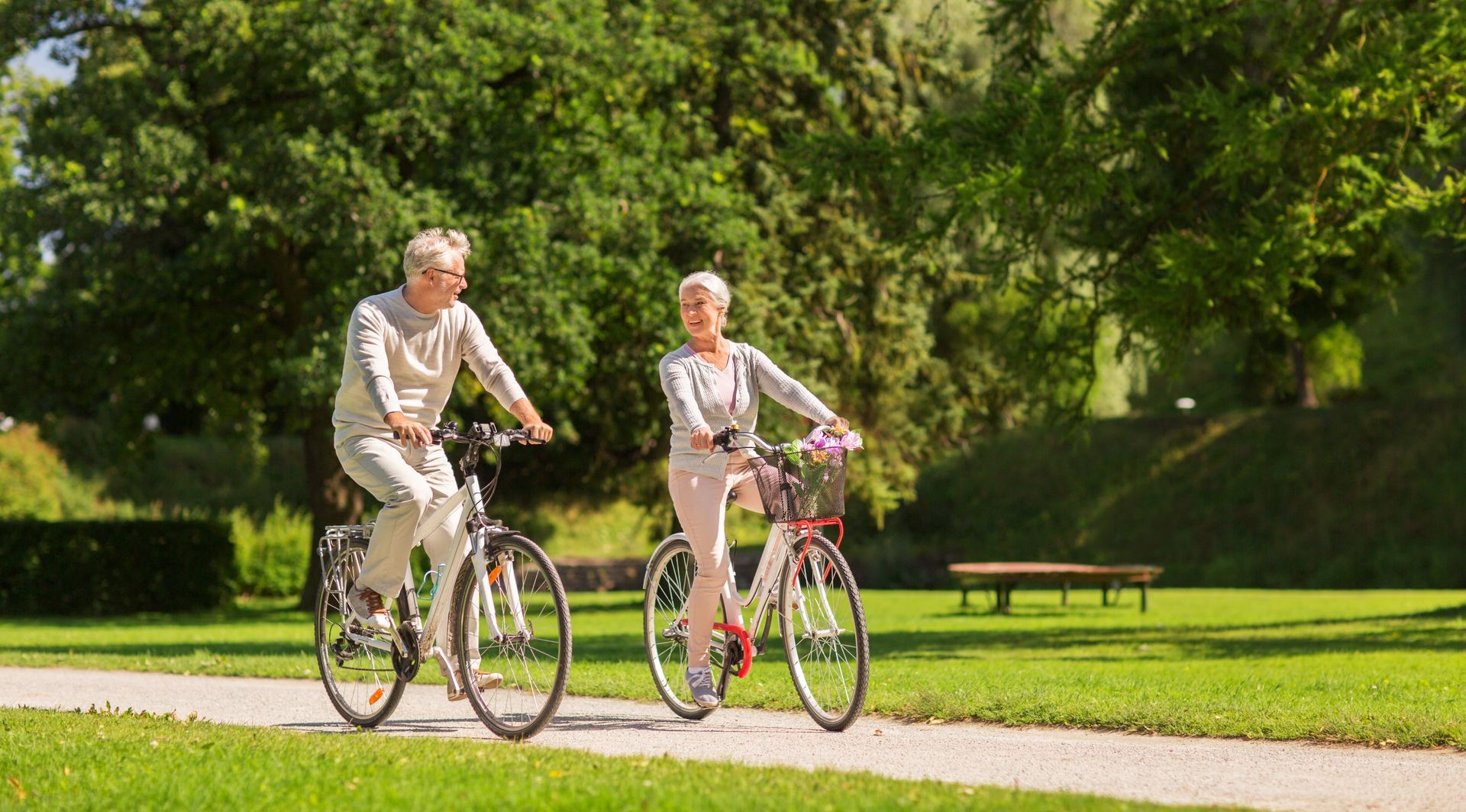 Zwei ältere Frauen fahren mit dem Fahrrad auf einem Weg in einem sonnigen Park.