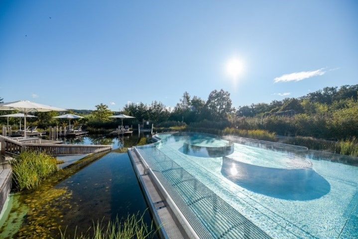 Outdoor-Spa mit blauen Pools und sonnigem Himmel. Wasserspiele sind von Grün umgeben.