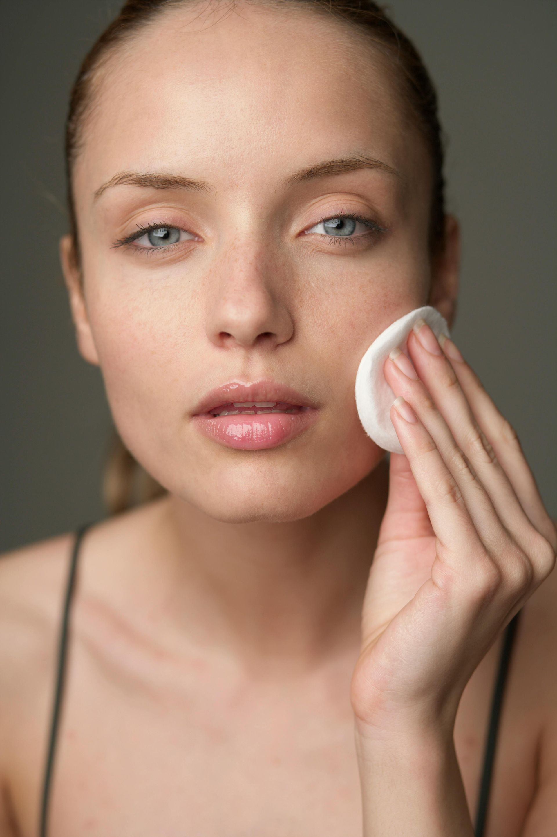 A woman with a towel wrapped around her head is applying a patch to her nose.