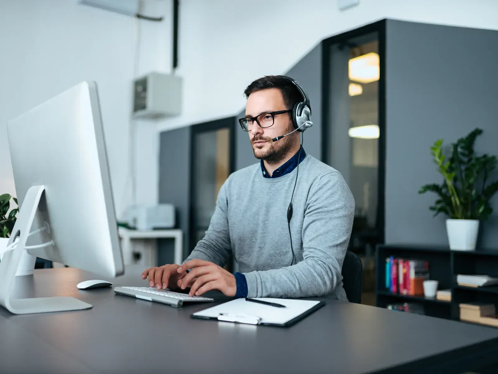 Person wearing a headset working at a desk in a modern office with a large monitor