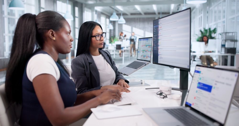 Two coworkers reviewing data on large monitors in a bright modern office