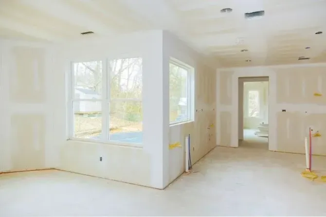 A room under construction with metal wall studs, drywall panels, and various tools placed on floor boards.