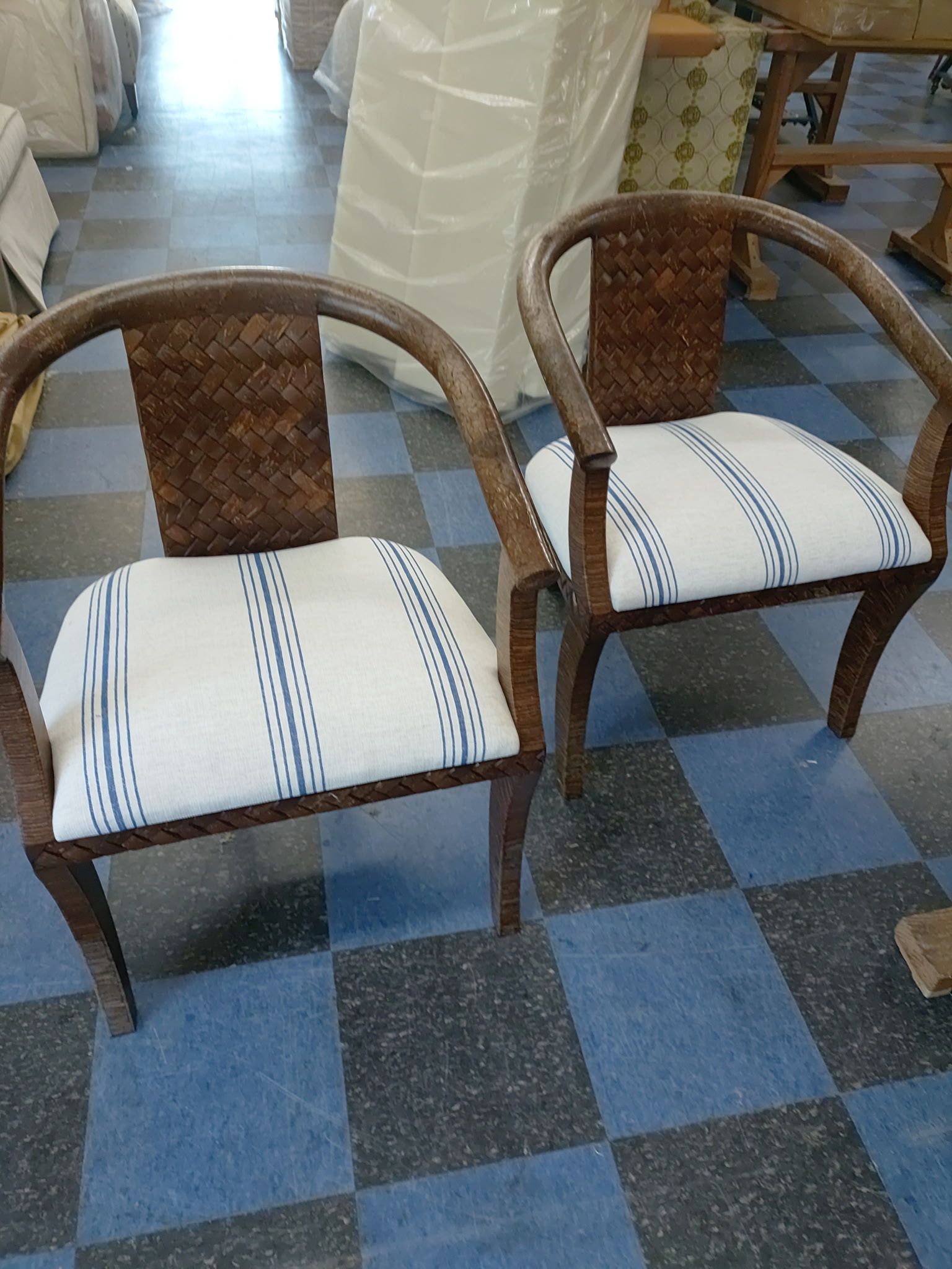 Two woven wooden chairs with white patterned cushions on a blue checkered floor in a room