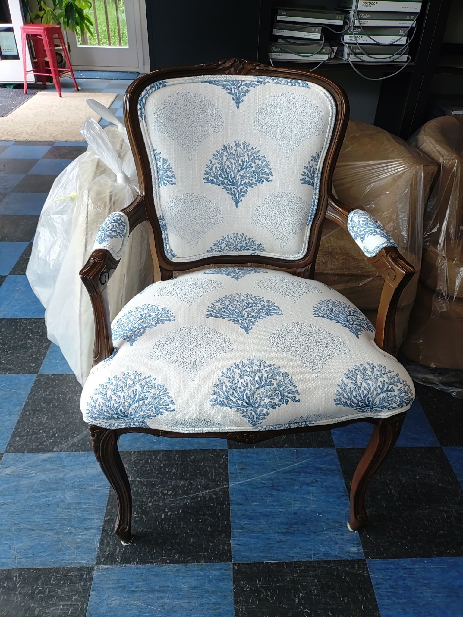 Vintage upholstered armchair with blue floral pattern and dark wood frame on a checkered floor