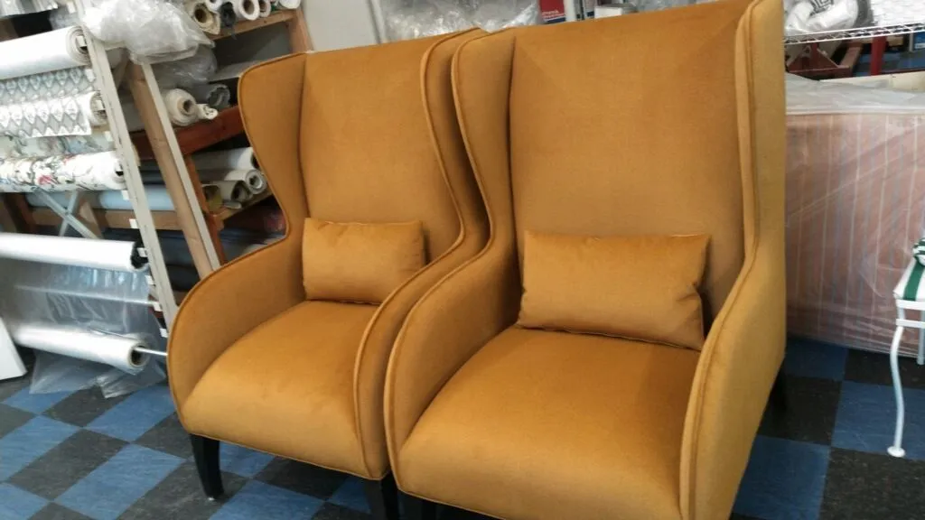 Two mustard-yellow wingback chairs with high backs and armrests in a furniture store.