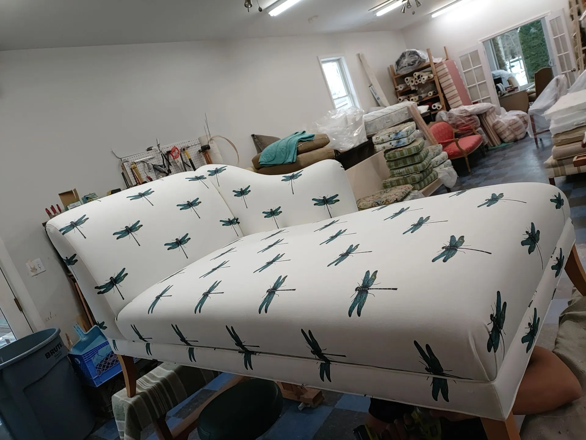 Living room with white patterned sofa, cushions, and stacked household items in the background