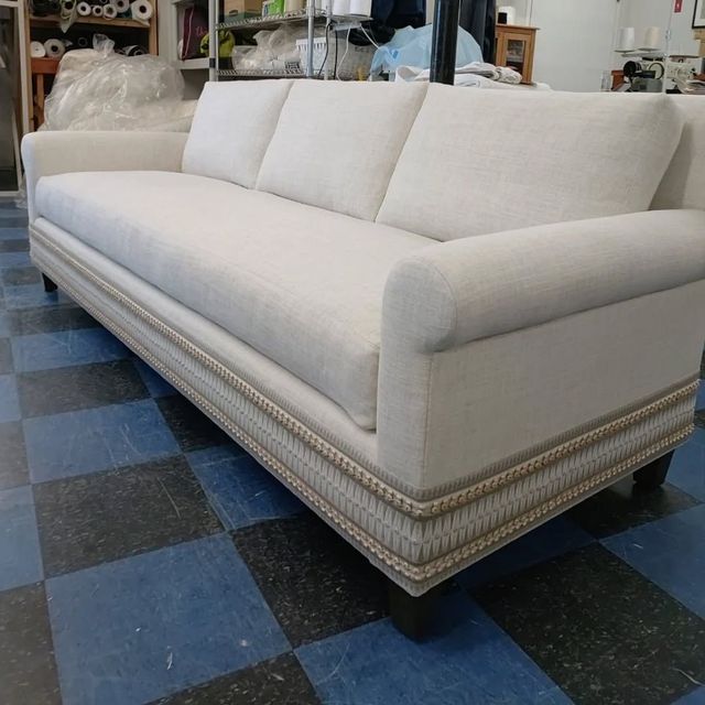 Cream upholstered sofa with nailhead trim on a blue checkered floor in a showroom