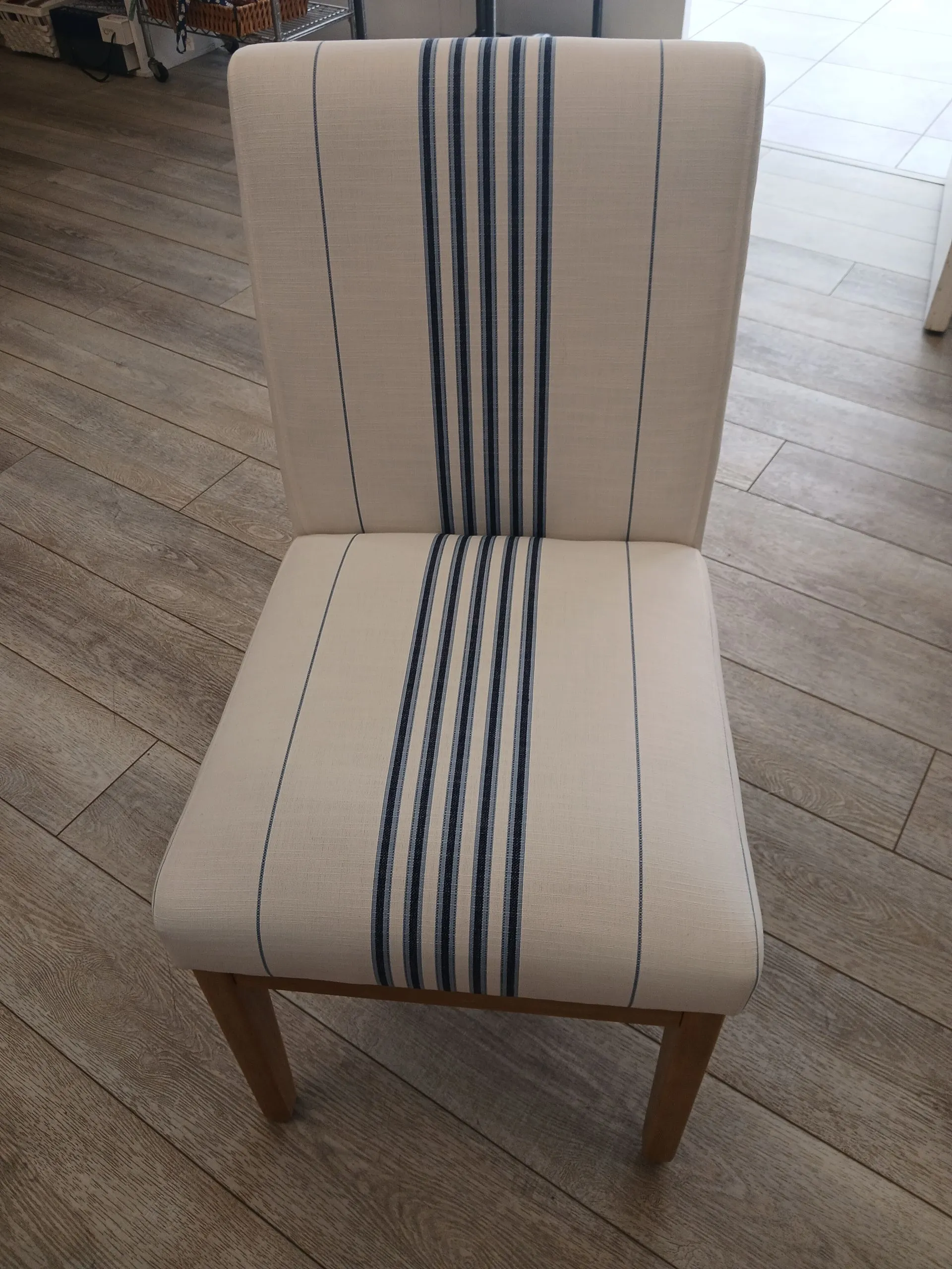 Beige upholstered chair with navy striped center, on a wooden floor.