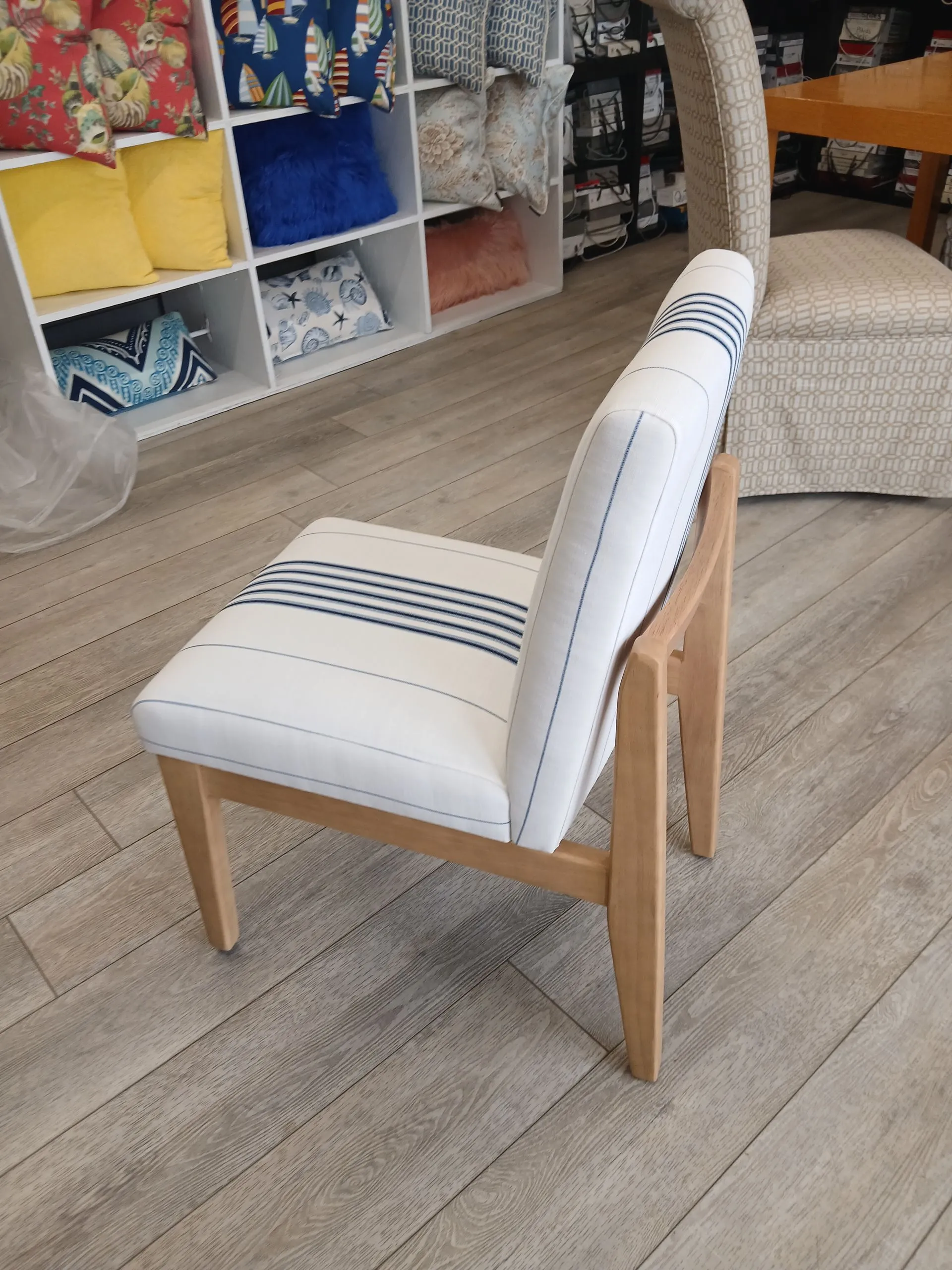 White striped chair with wooden legs on a light wood floor, in front of colorful cubby shelves and a scratching post