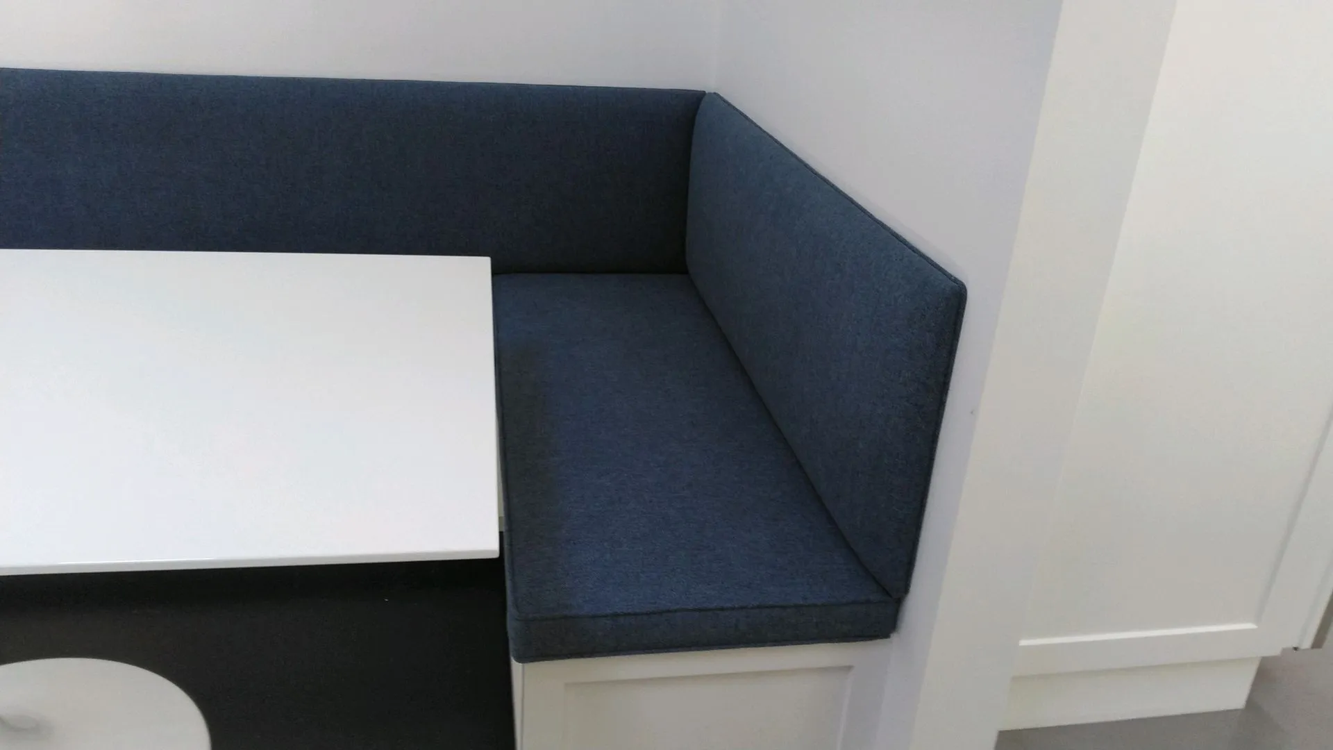 Blue upholstered booth bench beside a white table in a bright corner