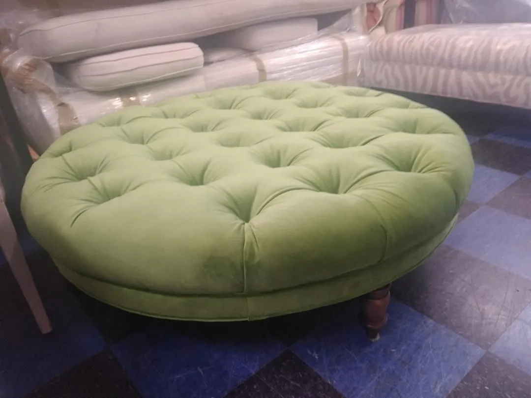 Green tufted round ottoman on a blue checkered floor in a room with bedding in the background