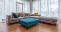 Modern living room with a gray sectional sofa and teal ottoman near bright windows