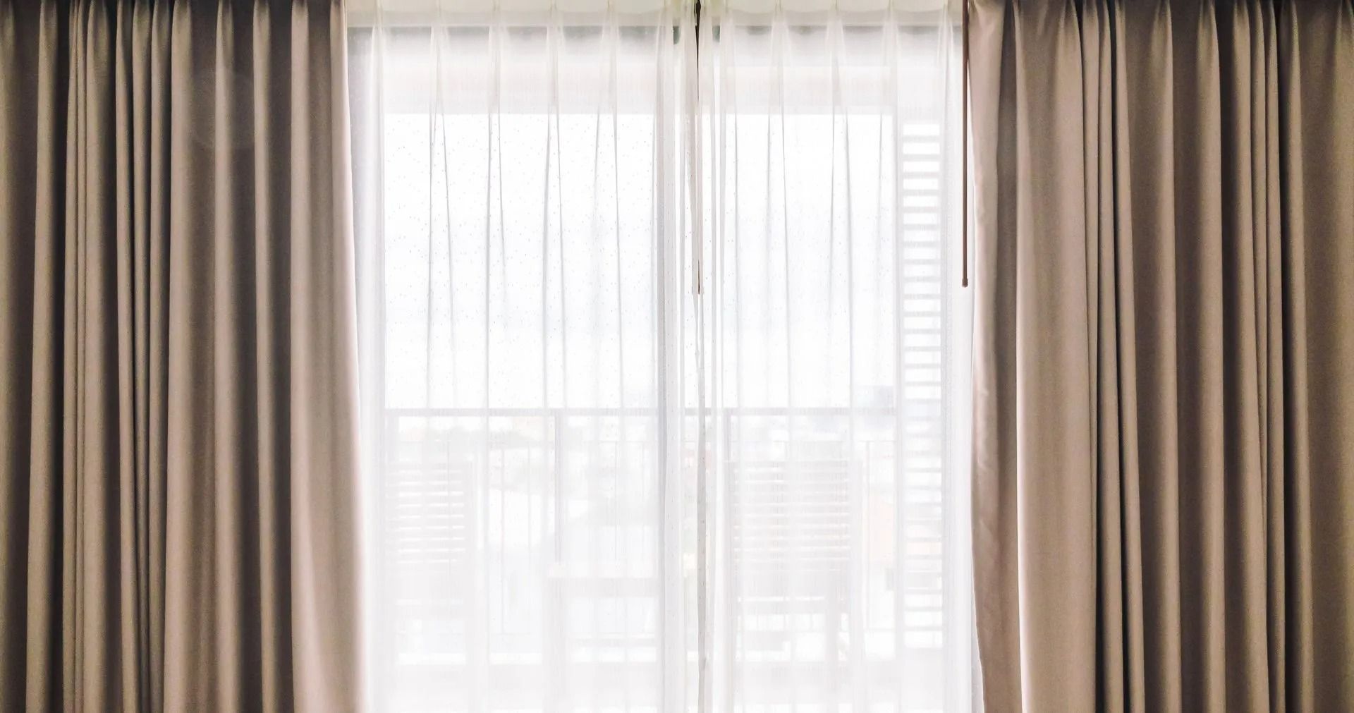 Sheer white curtains framed by beige drapes over a bright window in a softly lit room