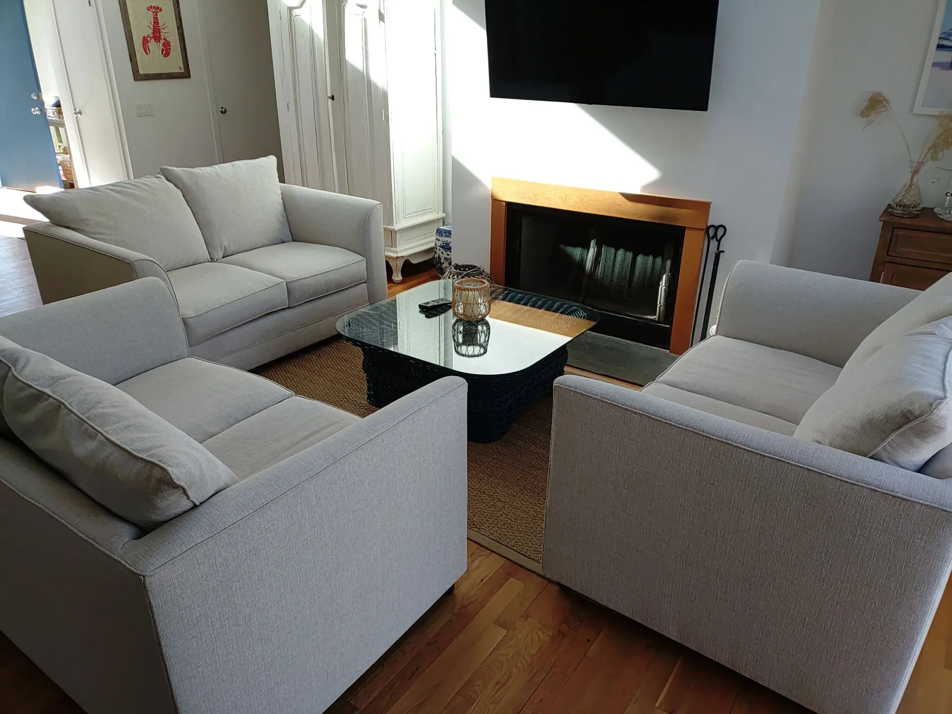 Bright living room with gray sofas around a glass coffee table and a fireplace beneath a wall-mounted TV.