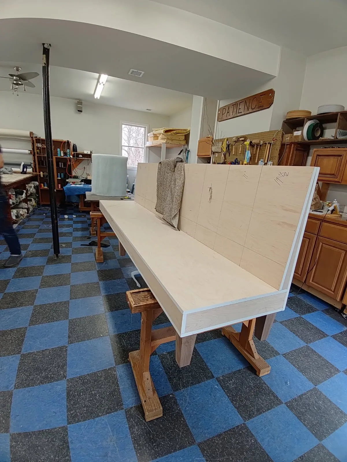 Workshop with a long white workbench and shelves of tools on a blue checkered floor.