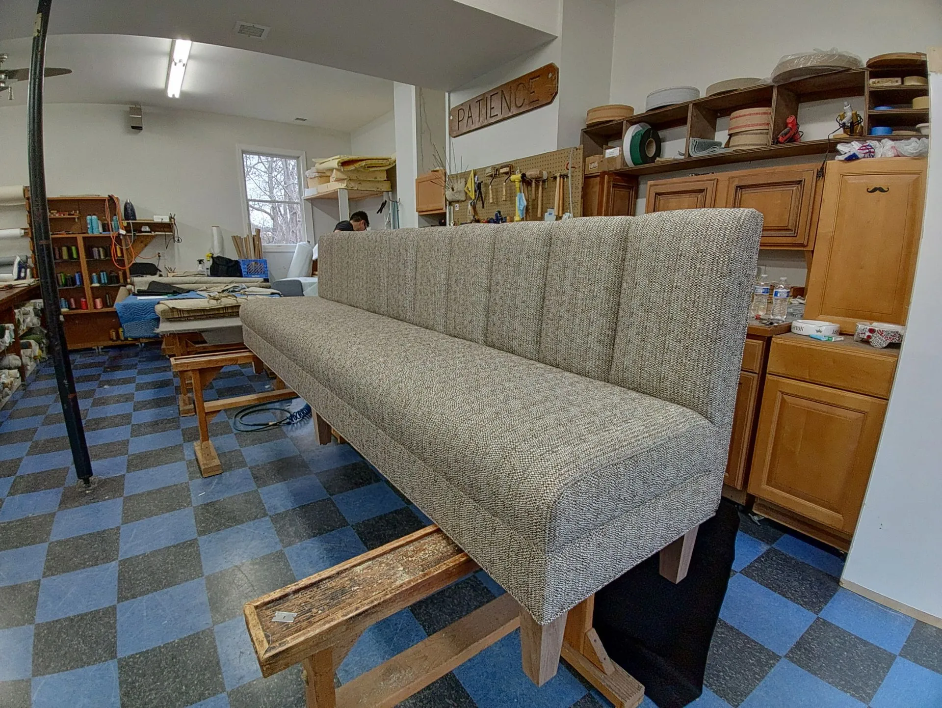 Long floral upholstered bench in a workshop with blue checkered floor and wooden cabinets