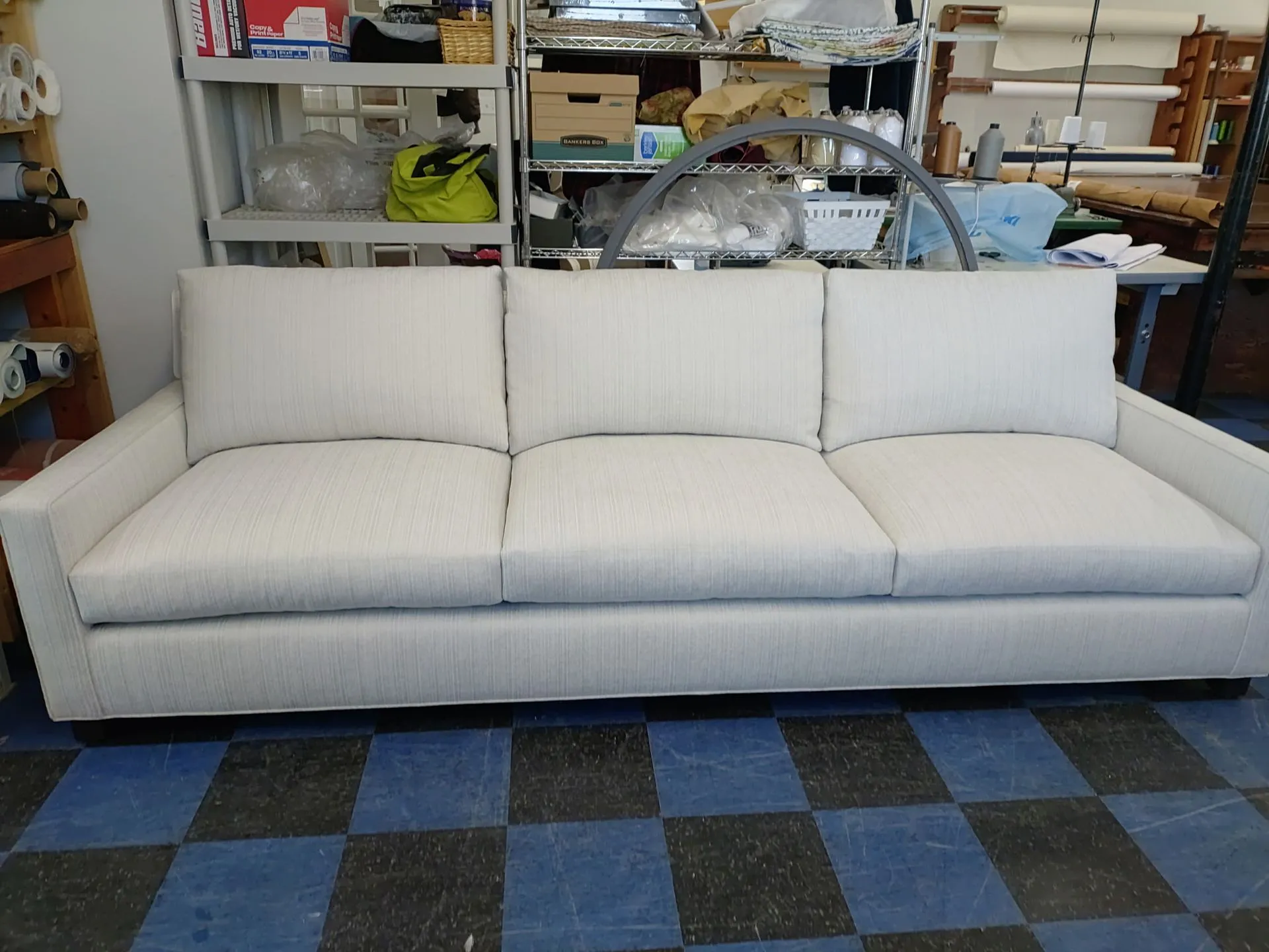 White three-seat sofa on a blue-and-black checkered floor in a workshop or storage room.