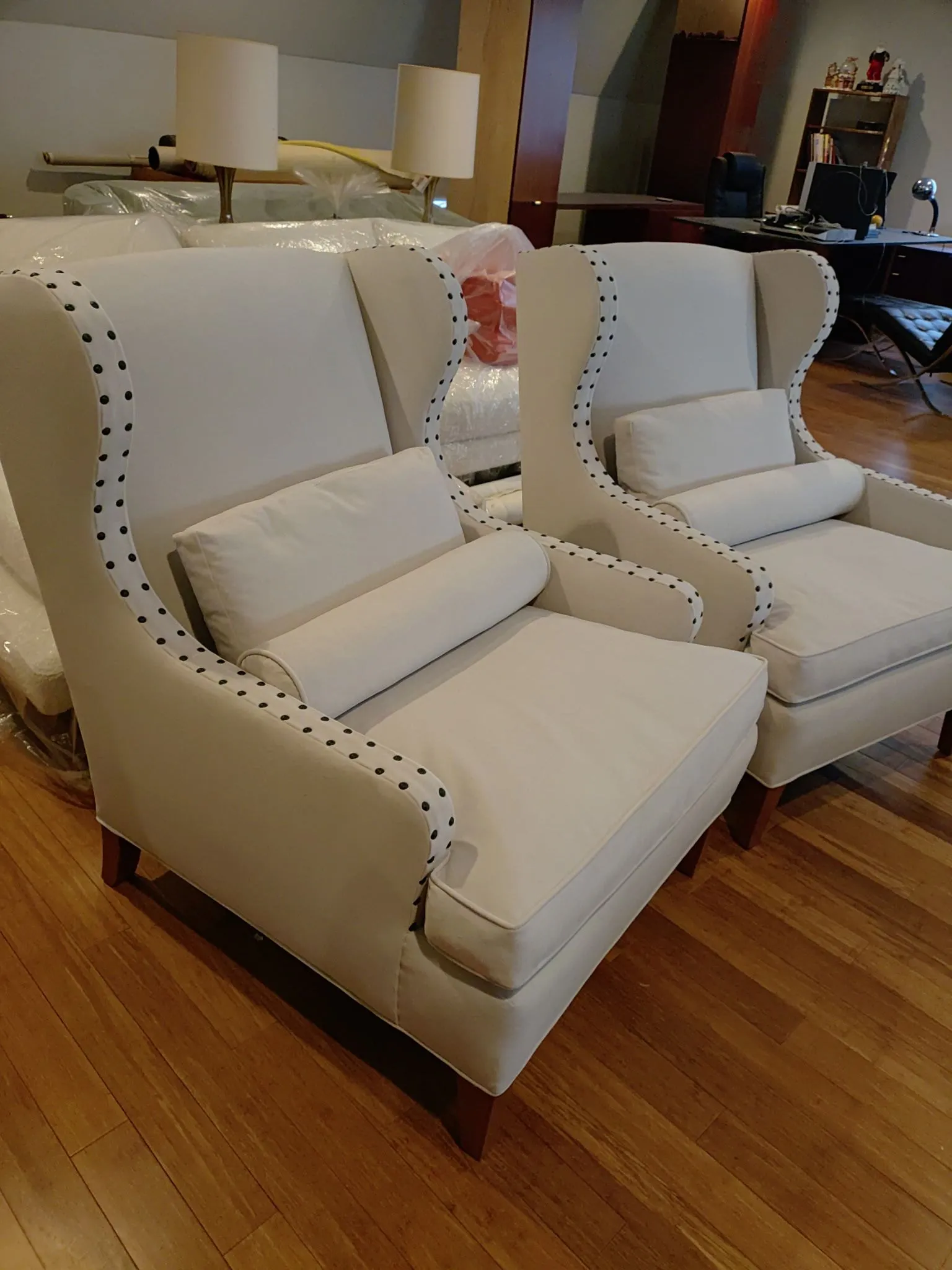 Two white upholstered armchairs with nailhead trim in a living room on a wooden floor