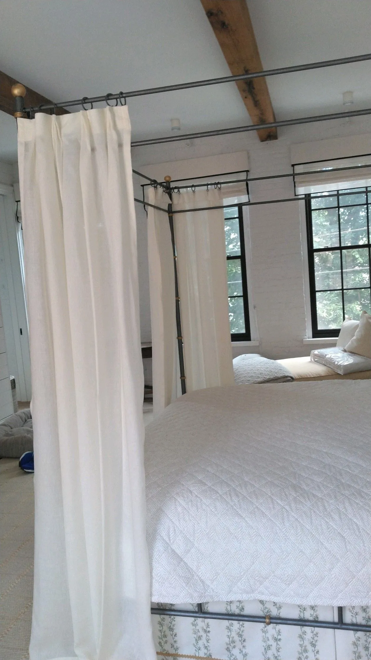 White-curtained bed in a bright room with exposed beams and windows.