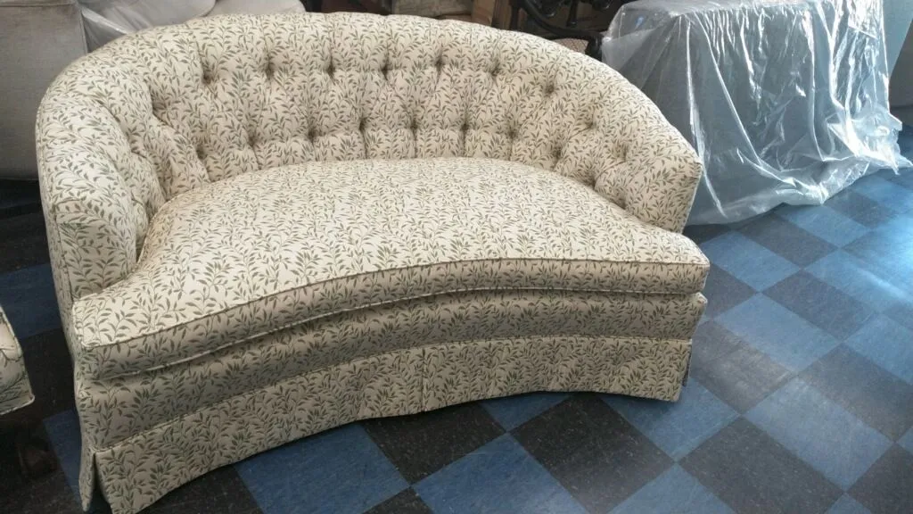 Cream tufted curved loveseat on a blue checkered carpet in a furniture store