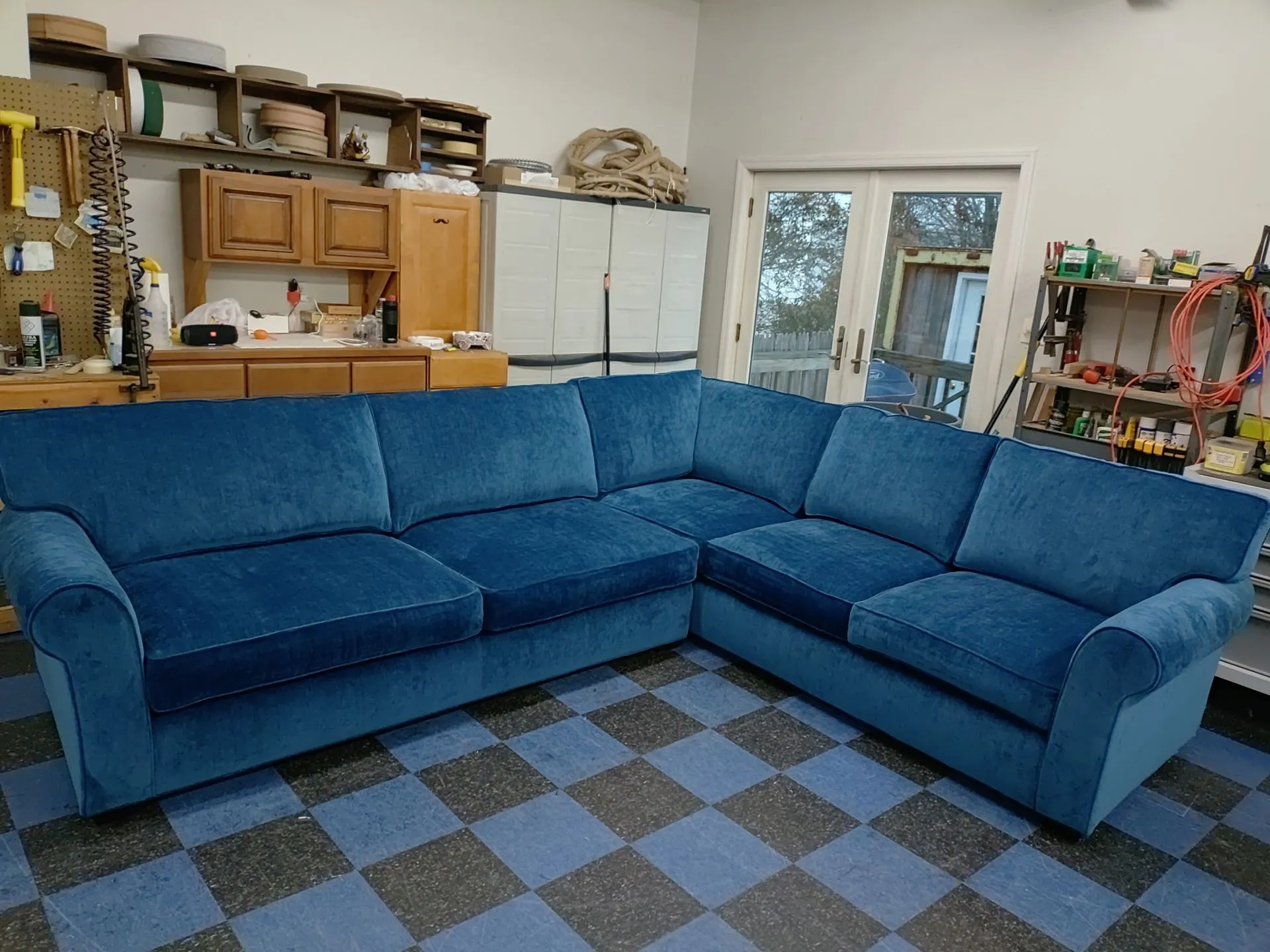 Blue sectional sofa in a garage or workshop with cabinets, white refrigerator, and checkered floor mat.