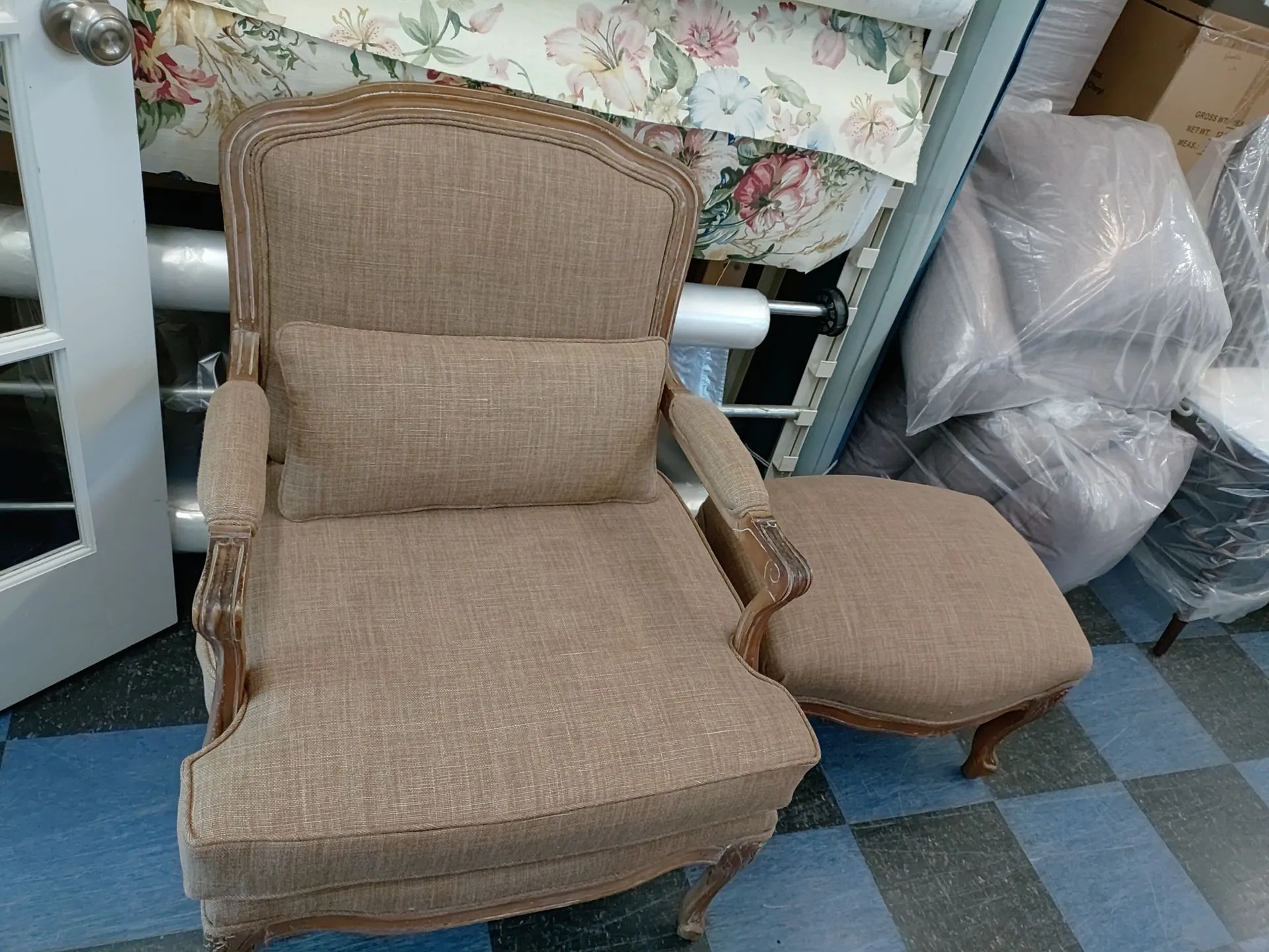 Cushioned wicker chair and matching ottoman beside a floral-covered bed in a room with blue checkered carpet