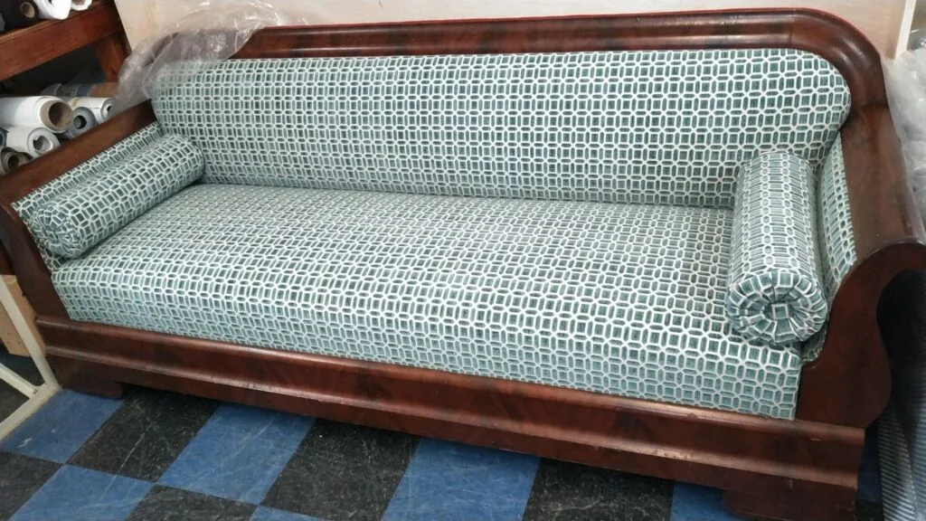 Brown wooden sofa with patterned green-and-white upholstery on a checkered floor