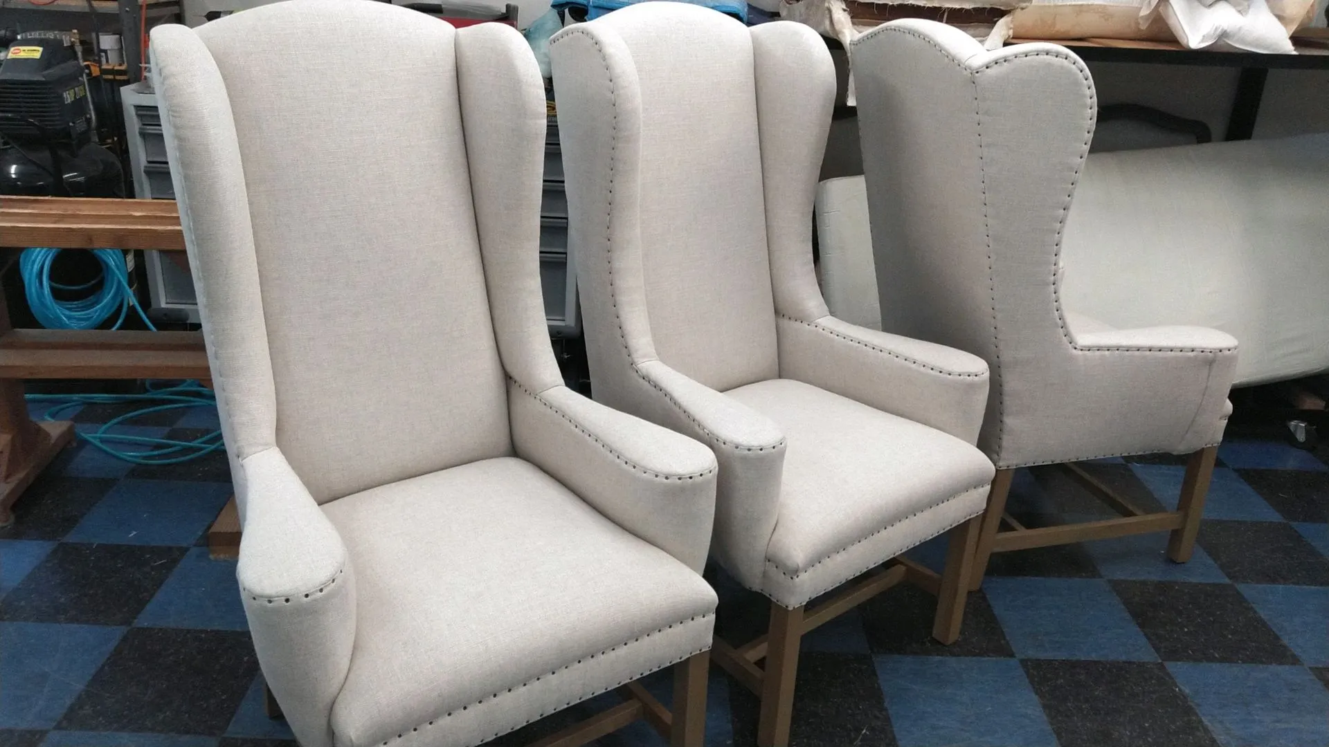 Three white upholstered wingback chairs lined up on a blue checkered floor