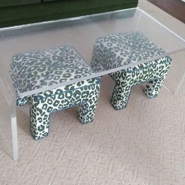 Two leopard-print animal-shaped ottomans under a glass-top table on a beige carpet.