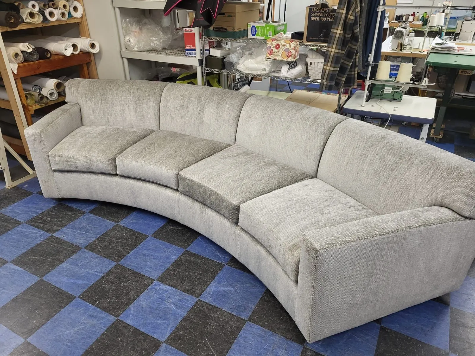 Curved light gray sectional sofa on a blue-and-black checkered floor in a workshop