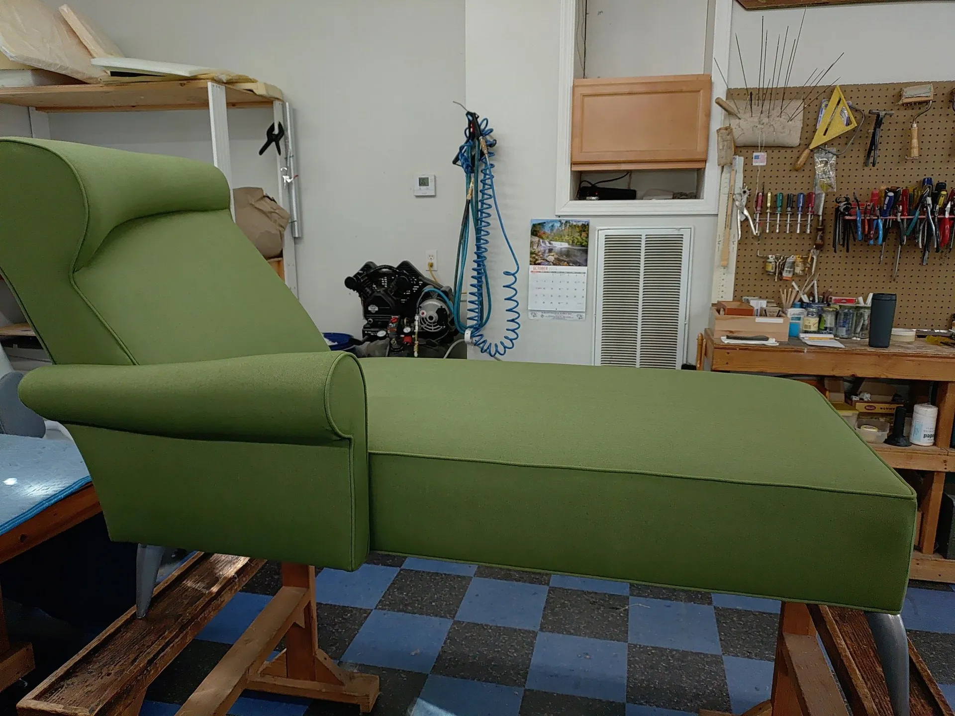 Green chaise lounge in a workshop garage with pegboard tools and storage shelves.