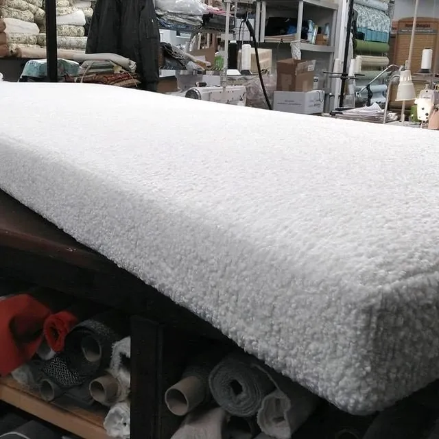 A thick white foam pad on a worktable in a workshop, with rolled materials stored underneath.