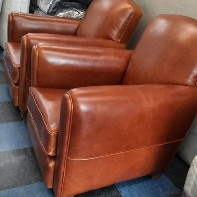 Two brown leather armchairs in a showroom or furniture store.