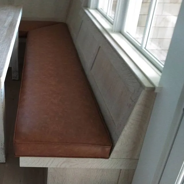 Long cushioned bench with brown seat under a window in a narrow alcove