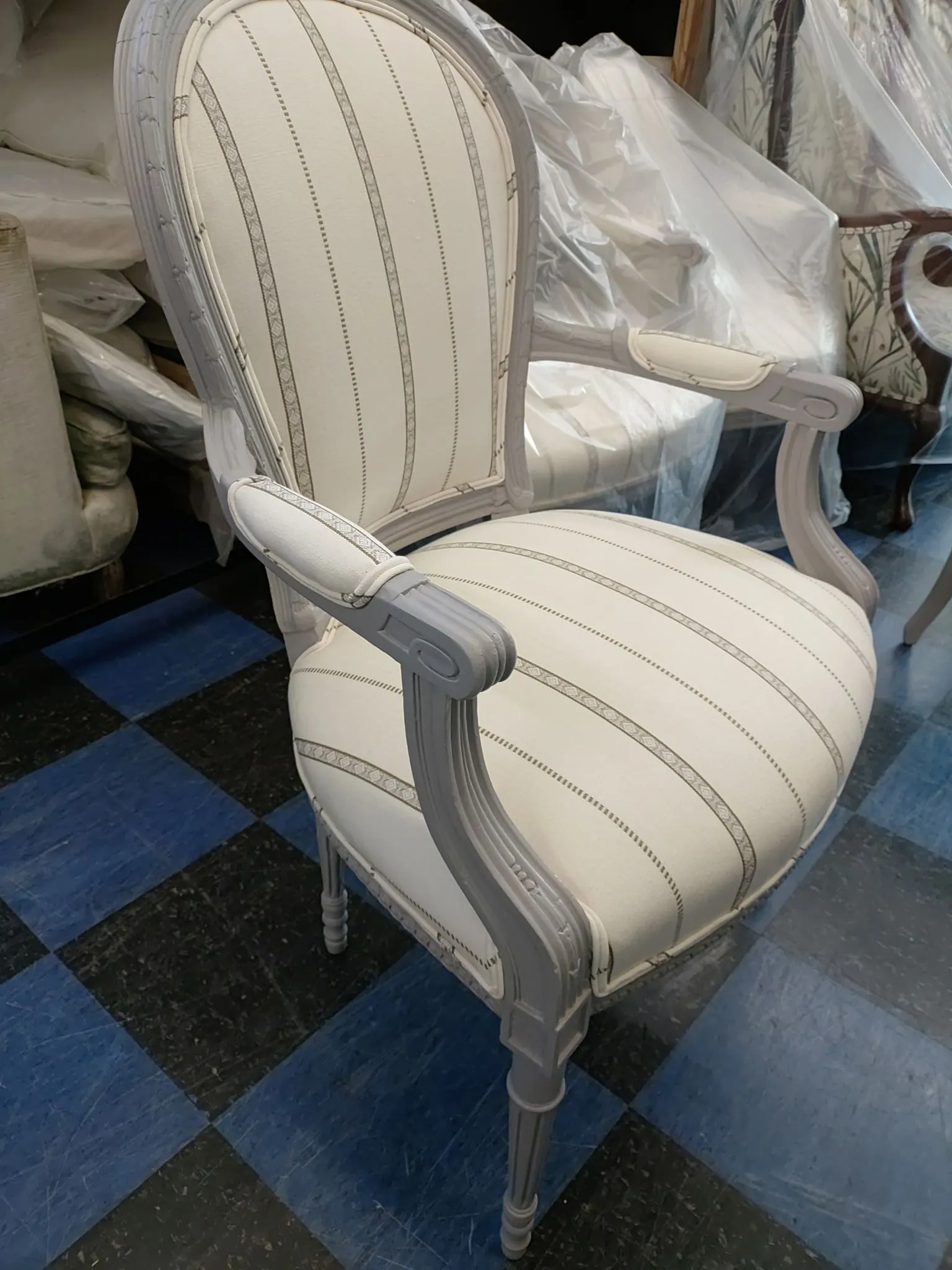 Cream upholstered vintage chair with striped fabric and carved white frame on a blue-black checkered floor