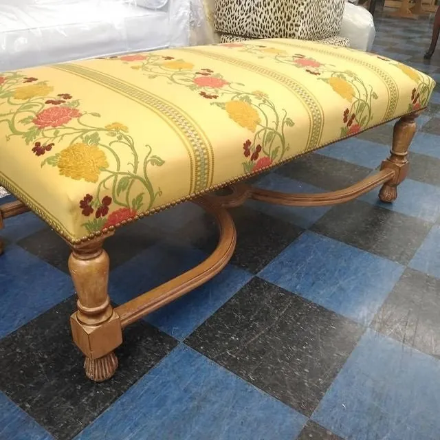 Yellow floral upholstered bench with carved wooden legs on a checkered floor