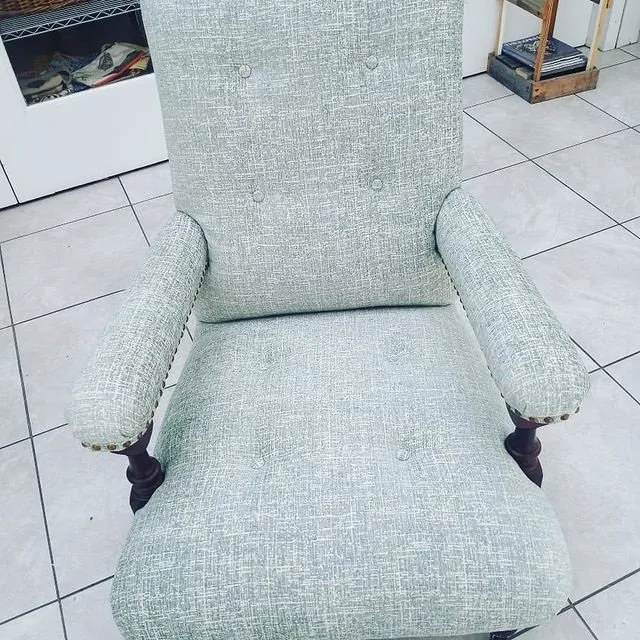 Light green upholstered armchair with armrests on a tiled floor indoors