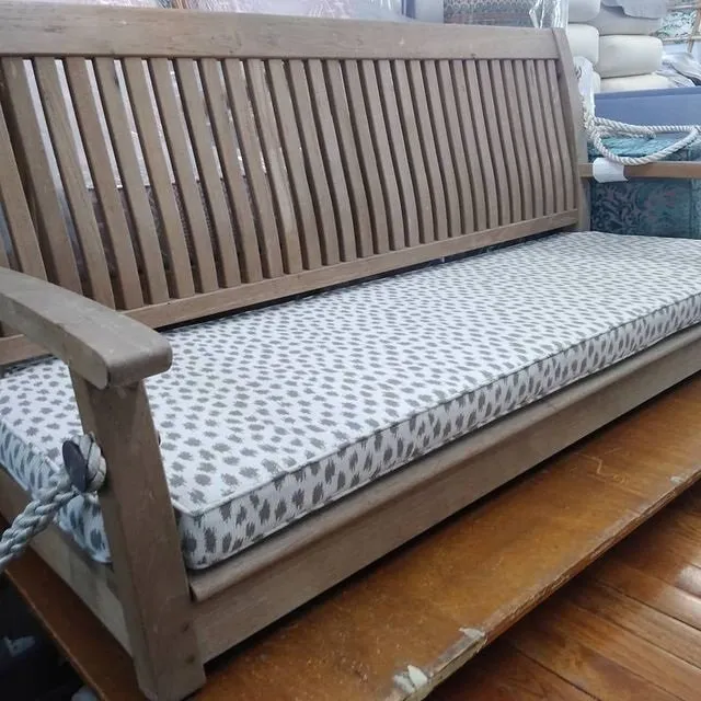 Wooden outdoor bench with gray patterned cushion on a wooden deck